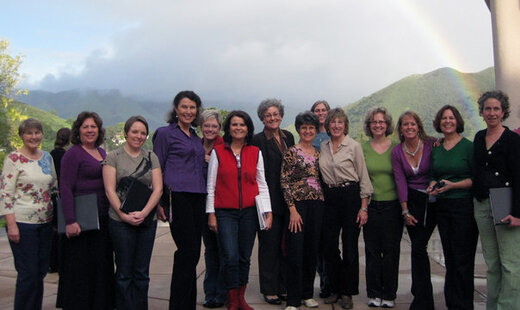 Canzona women's choir standing in front of green hills backdrop with rainbow in distance